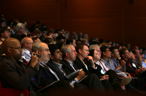 Professionally dressed people seated in an auditorium.