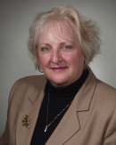 Professional portrait of Claudia A. Edwards wearing a tan suit jacket and black shirt.